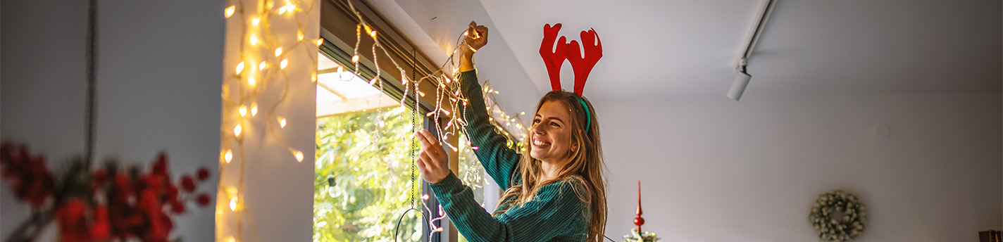 Eine Frau befestigt eine Lichterkette an Nägeln über einem Fenster