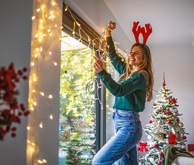Eine Frau befestigt eine Lichterkette an Nägeln über einem Fenster